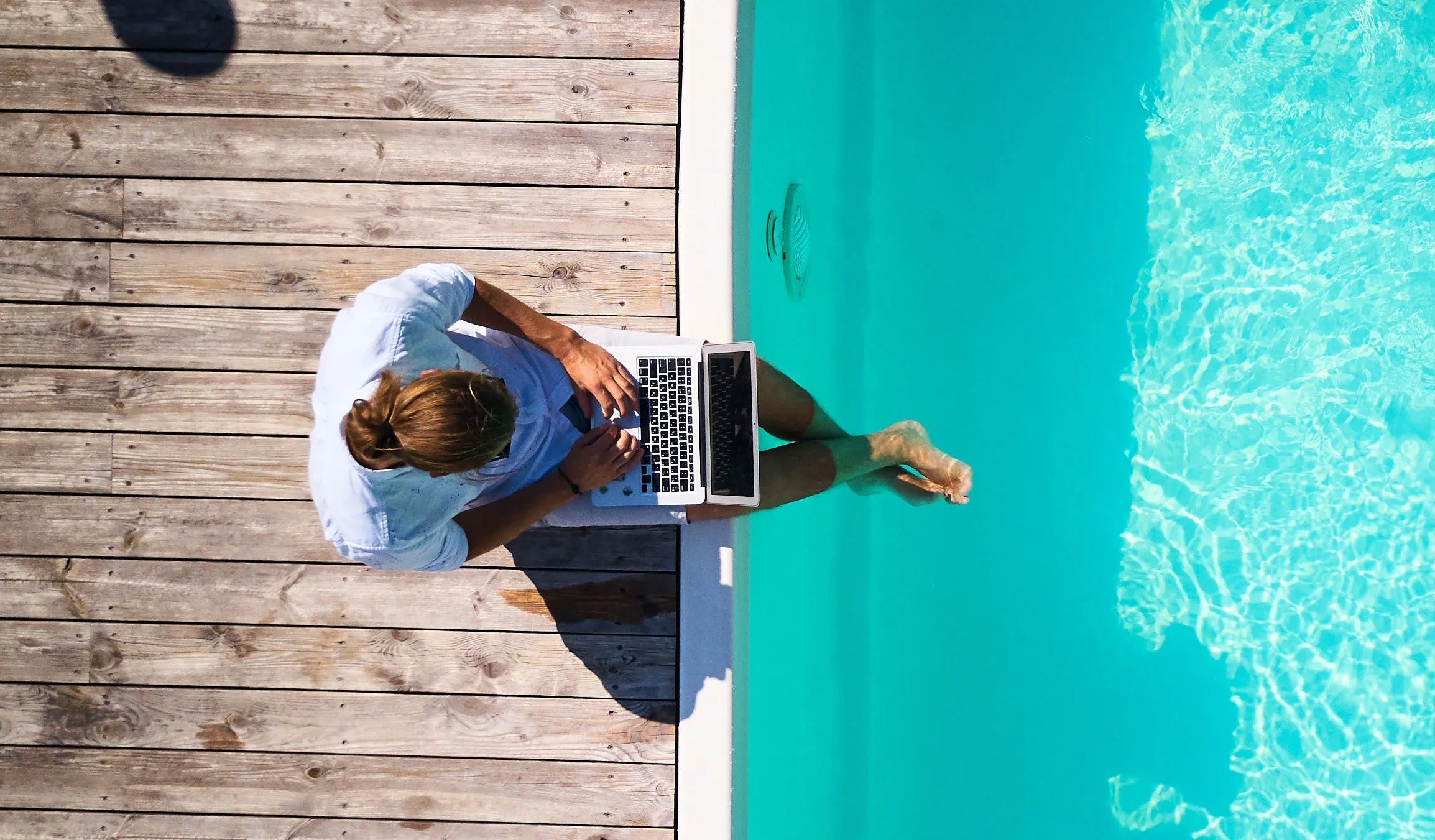 Man using laptop by pool edge