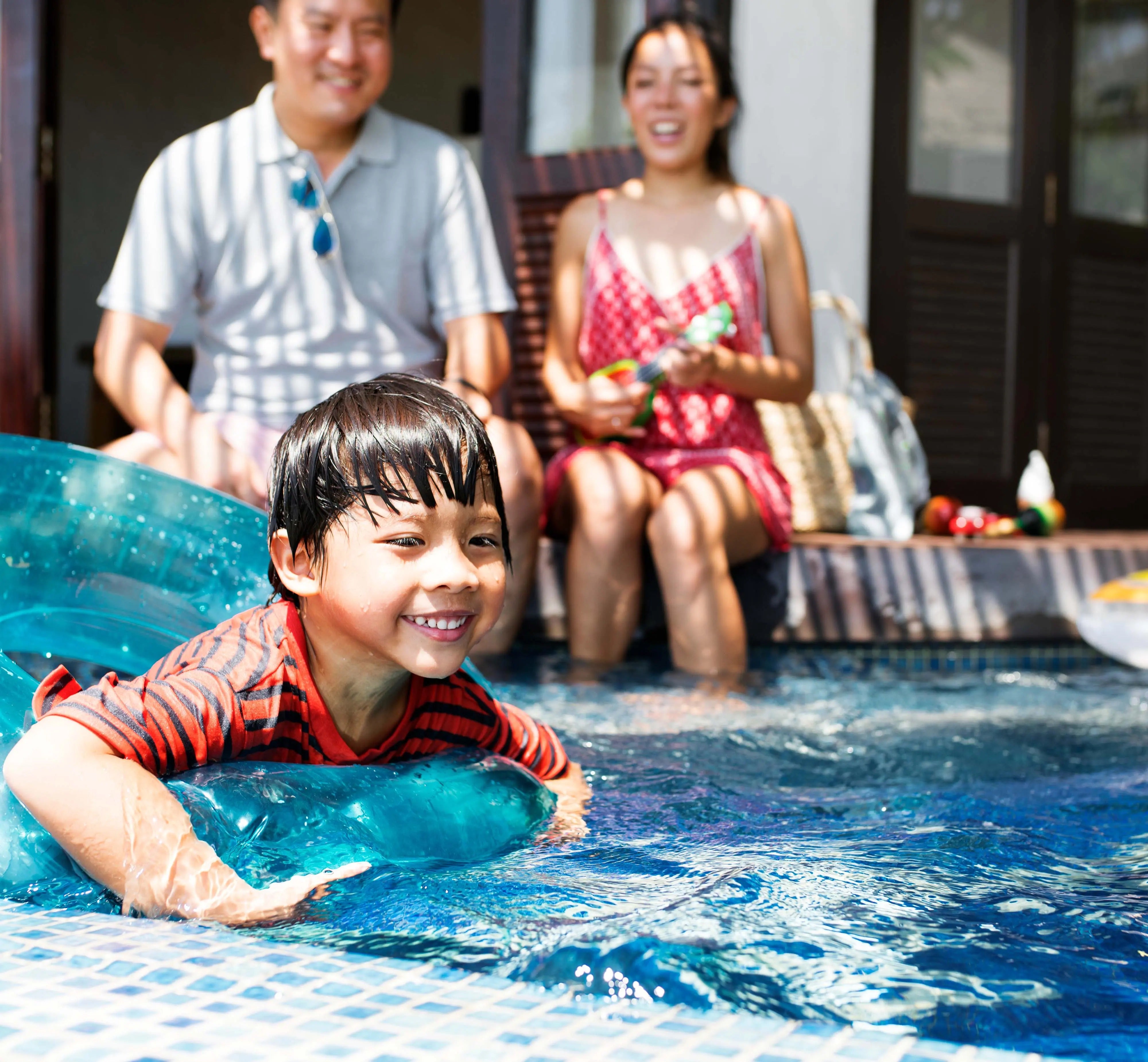 Child playing on an inflatable in the pool while his parents look on.